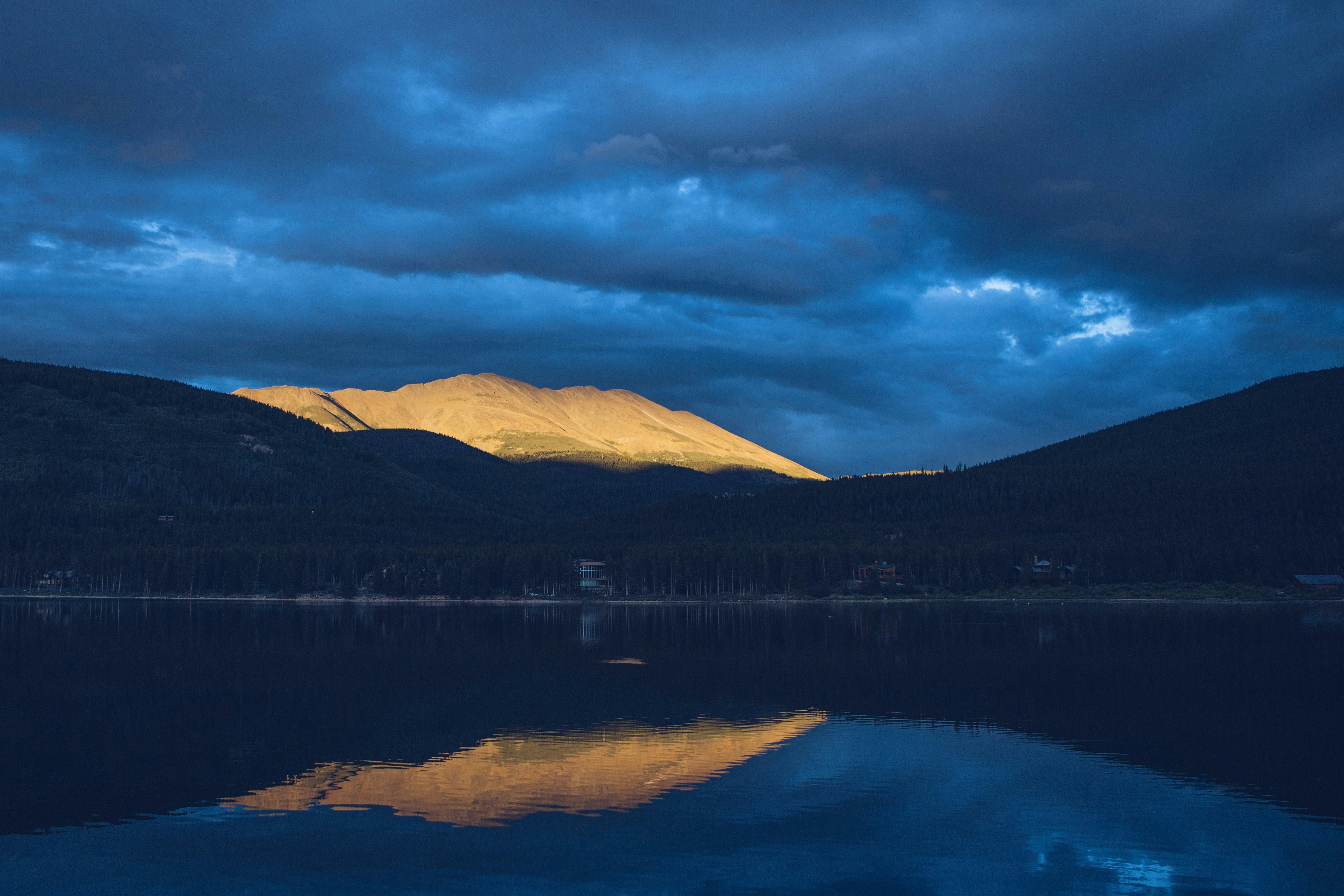 body of water near brown mountain under cloudy sky